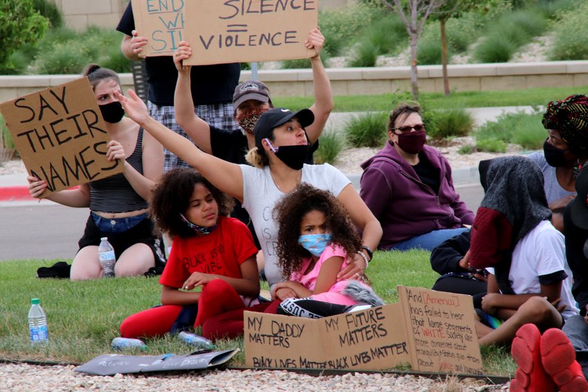 Valerie Carter, sitting with daughters Dominique, on the left, and Dionne, reacts to a heckler June 6 while sitting on the grass in front of the Northglenn Police station on Community Center Drive. The three were part of a group that marched peacefully from E.B. Rains Park to the Justice Center to protest for racial justice.